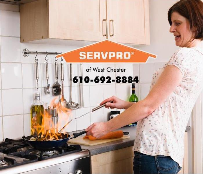 An anxious woman is cooking on a stovetop with flames rising out of control from the pan.